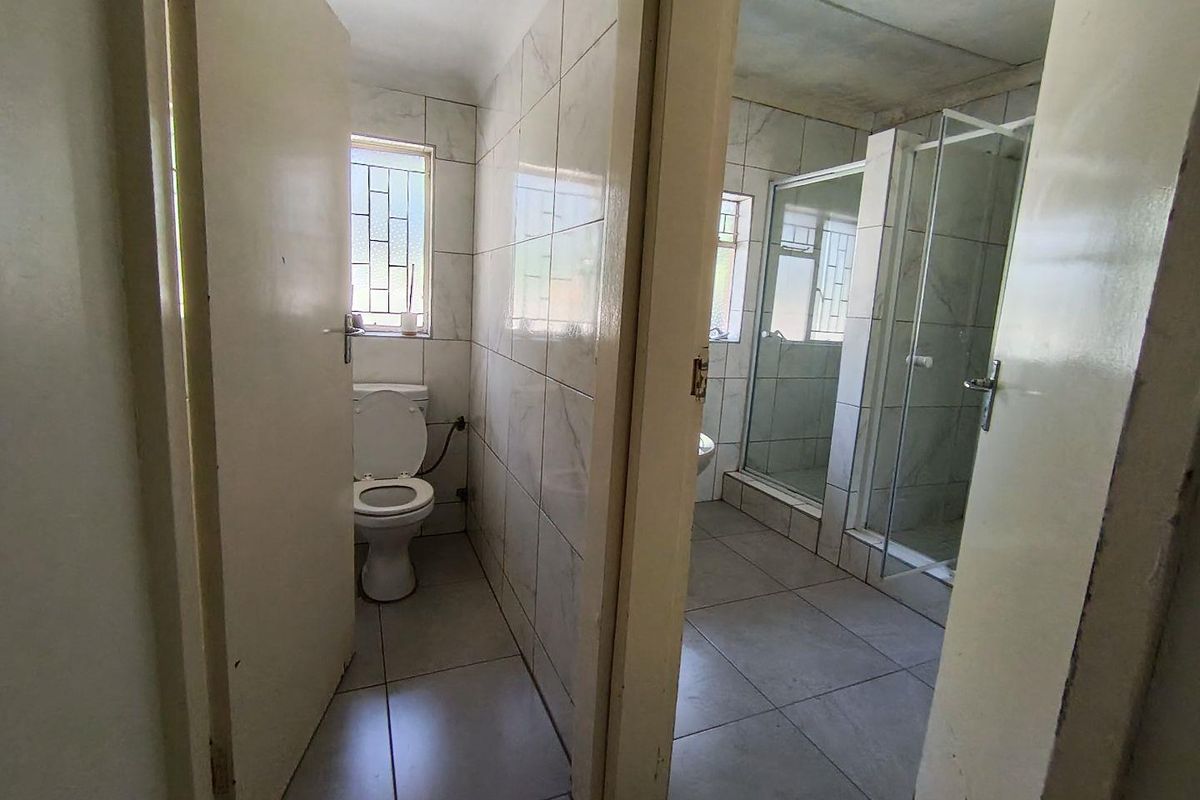 A functional bathroom featuring a separate toilet area and a glass-enclosed shower with neutral wall and floor tiling.