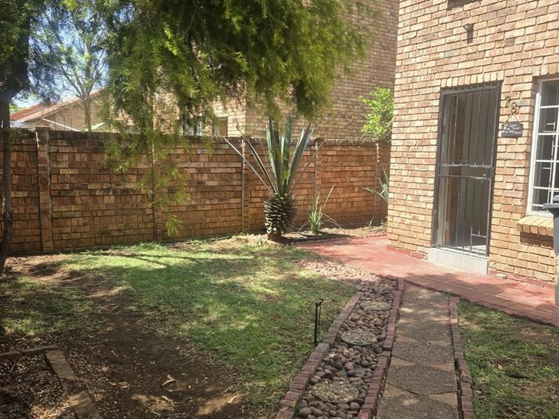 Rear garden area featuring a brick townhouse facade, security gate, paved walkway, and established boundary wall.