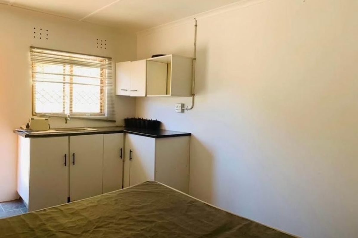 A compact kitchen area featuring basic built-in cabinetry, a laminate countertop, and a stainless steel sink, with visible exposed electrical conduit.