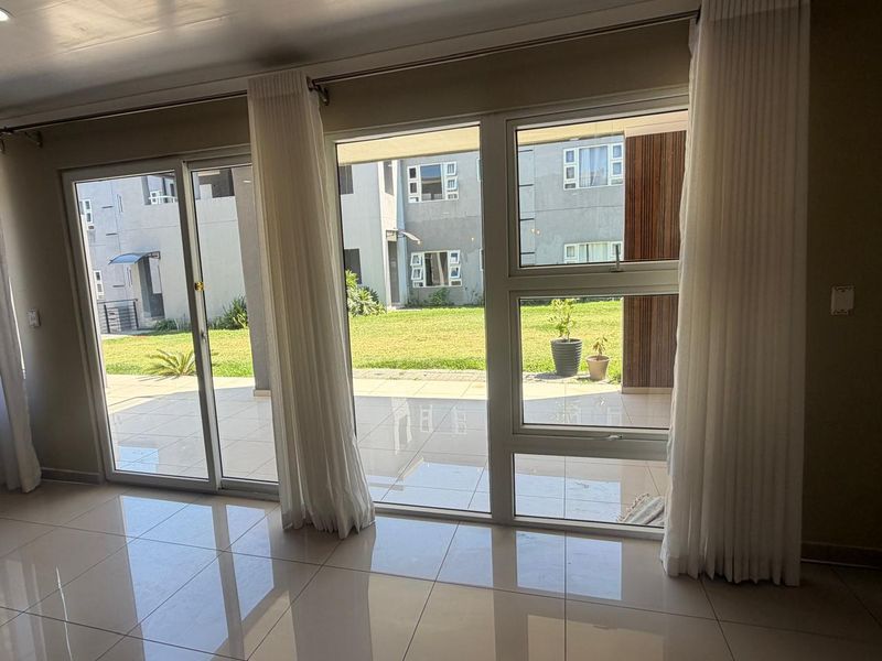 A bright and spacious living area featuring large sliding glass doors that open onto a patio, with polished tiled flooring throughout.