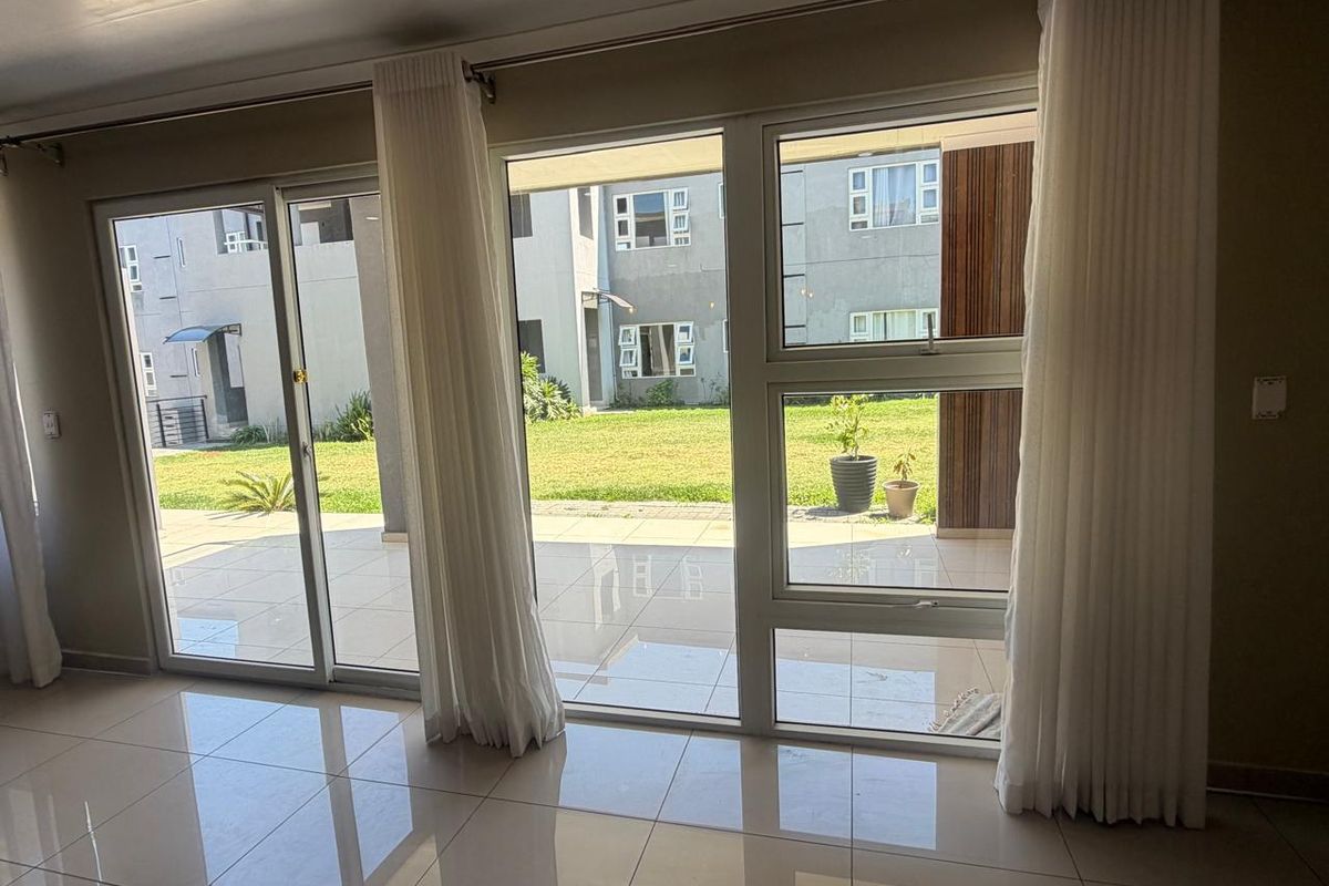A bright and spacious living area featuring large sliding glass doors that open onto a patio, with polished tiled flooring throughout.