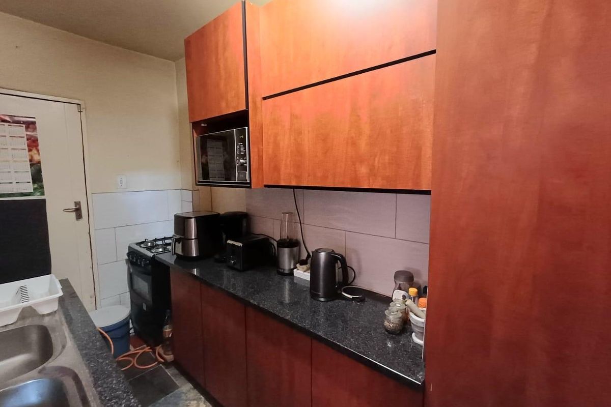 Compact kitchen featuring dark granite countertops, wood-veneer cabinetry, built-in microwave, and a gas stove with tiled backsplash.
