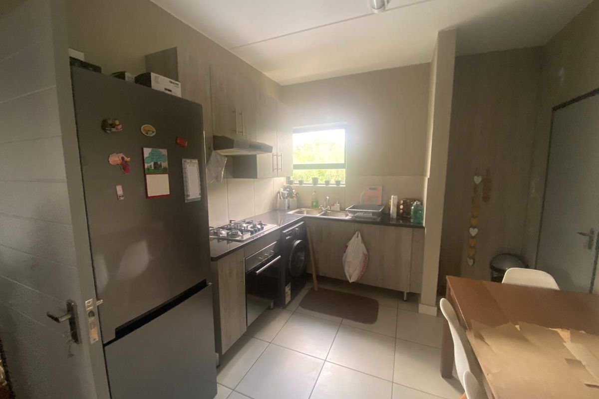 Compact kitchen featuring wood-look cabinetry, granite countertops, a gas hob, built-in oven, and integrated laundry plumbing, finished with neutral floor tiles.