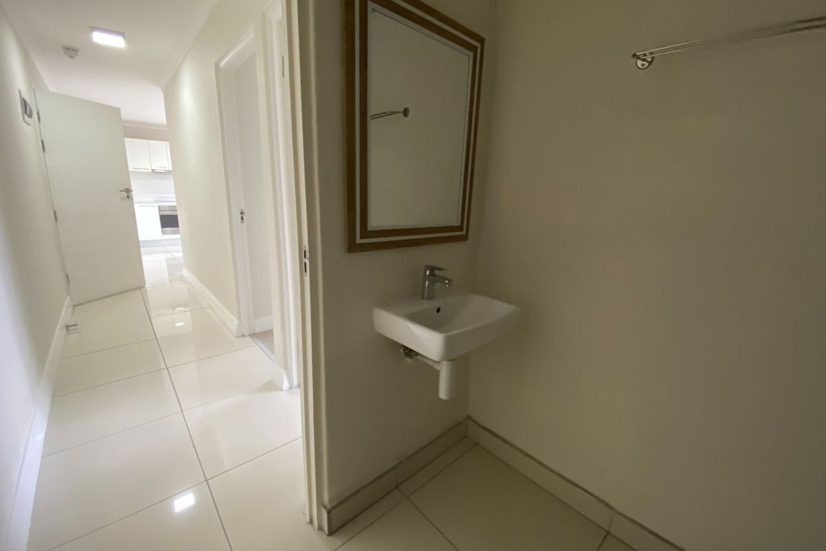 A compact guest bathroom featuring a wall-mounted basin, a framed mirror, and polished floor tiles, situated off the main hallway.