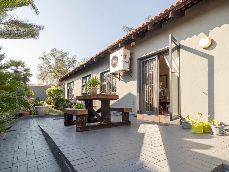 A paved outdoor patio area featuring an air conditioning unit, tiled roof overhang, and glass door access to the interior living space.
