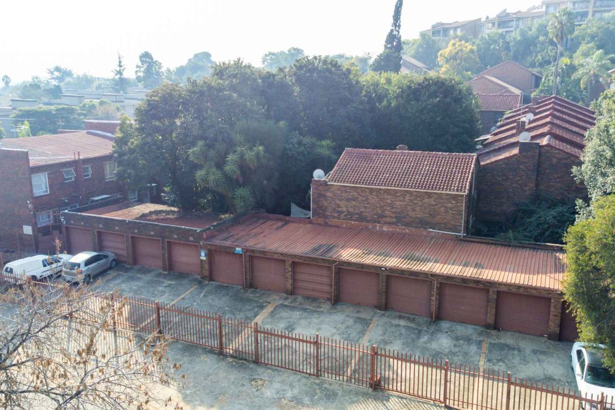 An elevated view of a residential apartment complex featuring a row of brick garages with tiled roofing and perimeter security fencing.