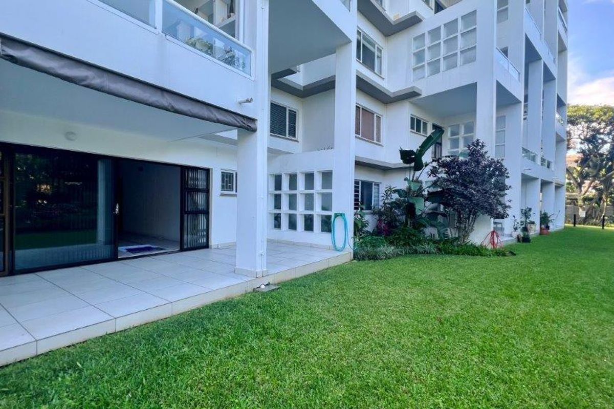 A ground floor apartment featuring a tiled patio area with sliding glass doors, overlooking a well-maintained communal garden and lawn.