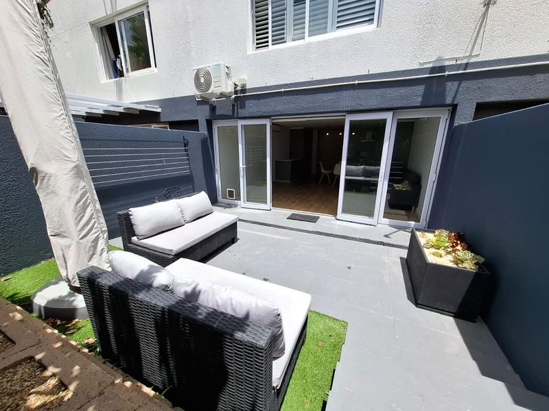 A well-maintained paved patio area featuring sliding glass doors, an external air conditioning unit, and a wall-mounted clothesline.