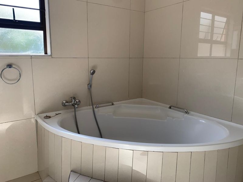 A functional bathroom featuring a corner bathtub with a handheld shower attachment and neutral wall tiling.