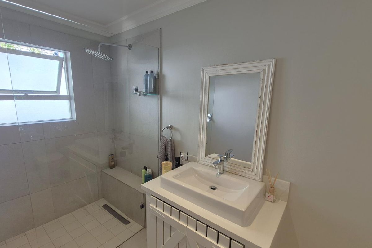 Modern bathroom featuring a walk-in shower with a rainfall showerhead, glass partition, and a single vanity with a basin.