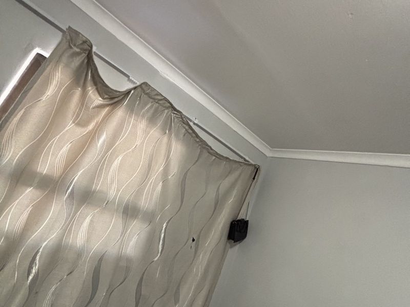 A corner view of a bedroom featuring coving and a curtain rail, showing neutral wall finishes.