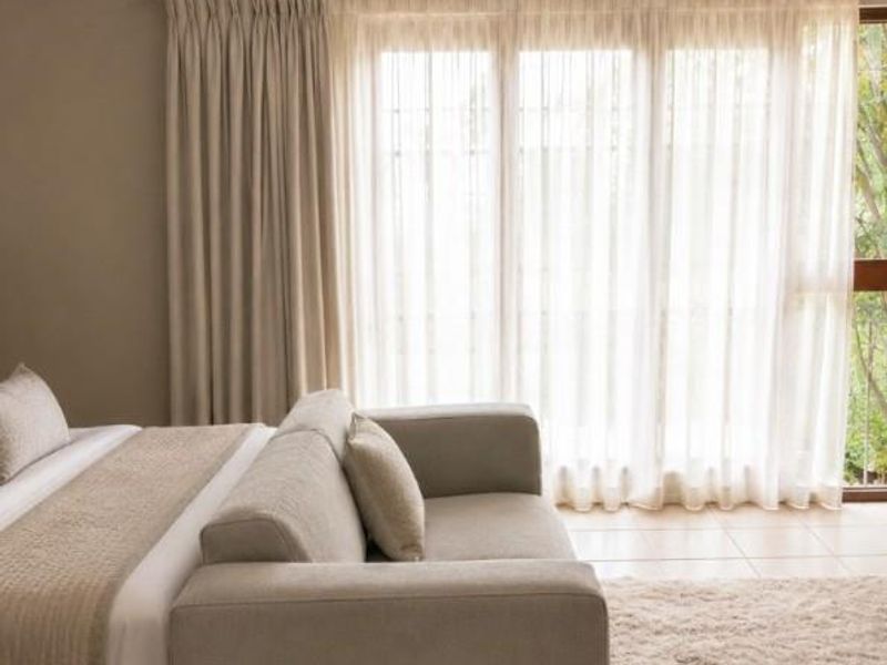 A well-lit bedroom featuring neutral tones, tiled flooring, and a large sliding glass door with floor-to-ceiling curtains providing access to the outdoors.