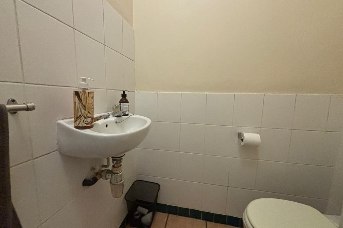 A compact office bathroom featuring a wall-mounted basin, toilet, and tiled finishes, currently showing signs of wear and dated fixtures.