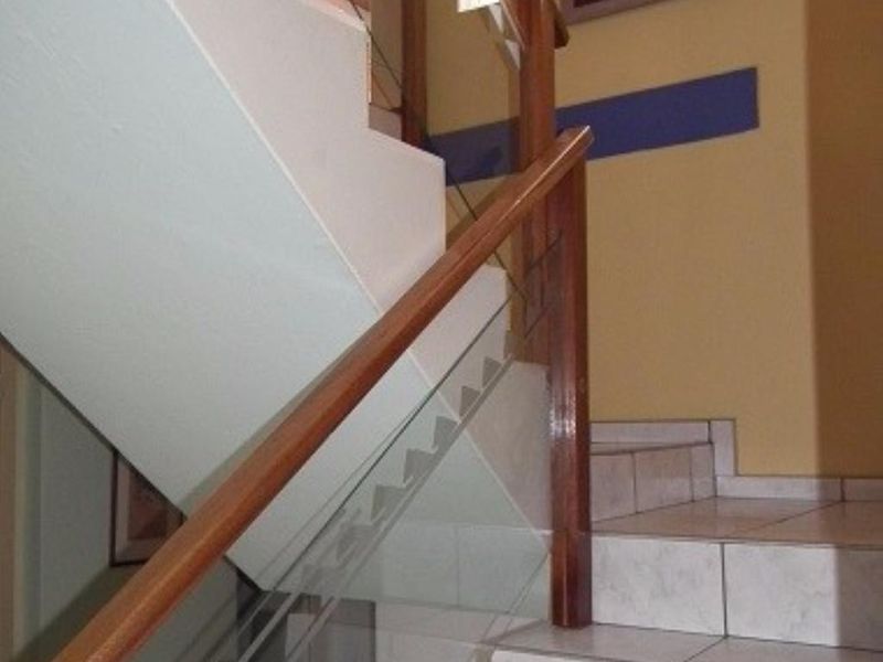 A staircase featuring tiled steps, a timber handrail, and a glass balustrade, providing access between levels.