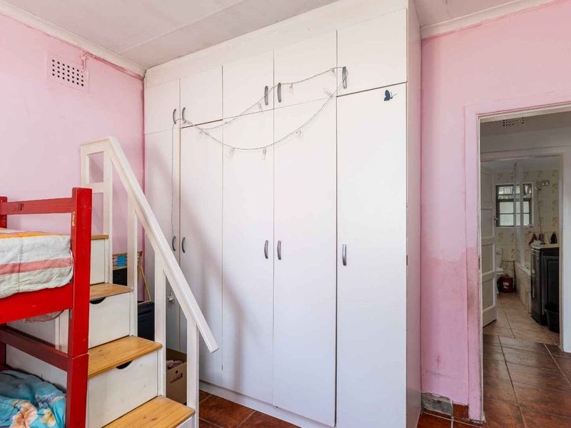 Bedroom featuring built-in white wardrobes, tiled flooring, and access to an adjoining bathroom. The room requires cosmetic updates to the wall finishes.