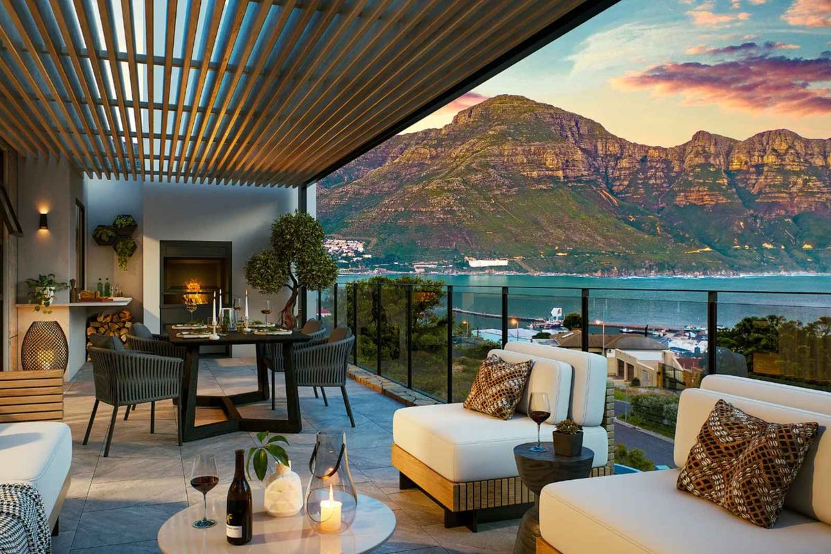 Spacious covered balcony featuring a built-in fireplace, slatted pergola, and glass balustrade, offering stunning panoramic mountain and coastal views.