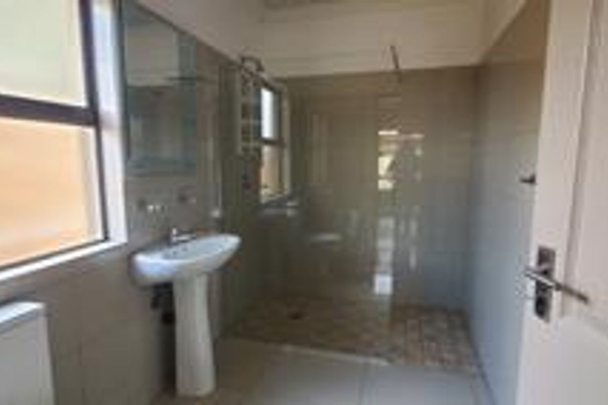 A functional bathroom featuring a pedestal basin, a walk-in shower with a glass screen, and neutral wall tiling.