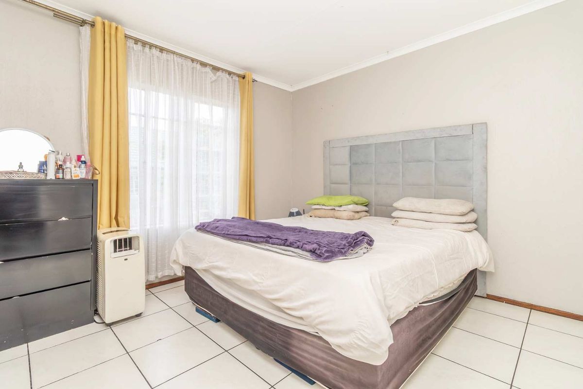 A functional bedroom featuring tiled flooring and large windows with curtain rails, providing a neutral base for personalization.