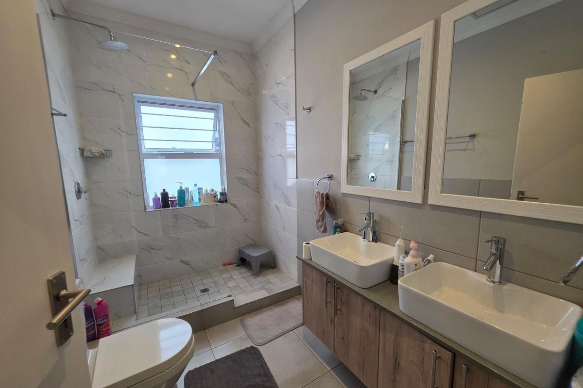Modern bathroom featuring a walk-in shower with marble-look tiling, dual vessel sinks on a wood-finish vanity, and contemporary fixtures.
