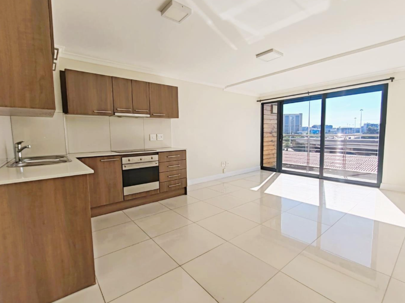Bright open-plan kitchen and living area featuring modern cabinetry, built-in appliances, tiled flooring, and large sliding doors leading to a balcony.