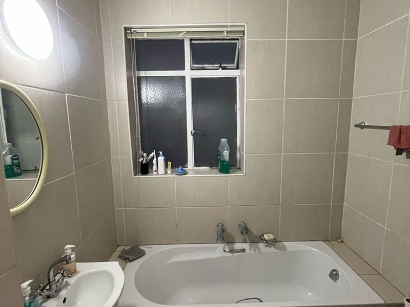 A functional bathroom featuring a built-in bathtub, vanity basin, toilet, and neutral wall tiling throughout.