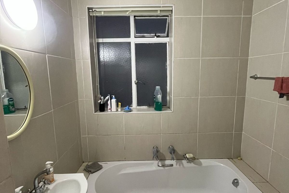 A functional bathroom featuring a built-in bathtub, vanity basin, toilet, and neutral wall tiling throughout.