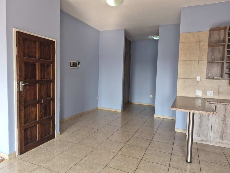 An open-plan living and kitchen area featuring neutral tiled flooring, built-in cabinetry, and a solid timber entrance door.
