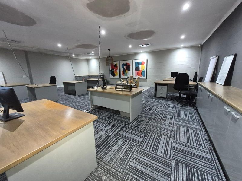 Open-plan office space featuring carpet tile flooring, recessed downlighting, and built-in storage cabinetry along the wall.