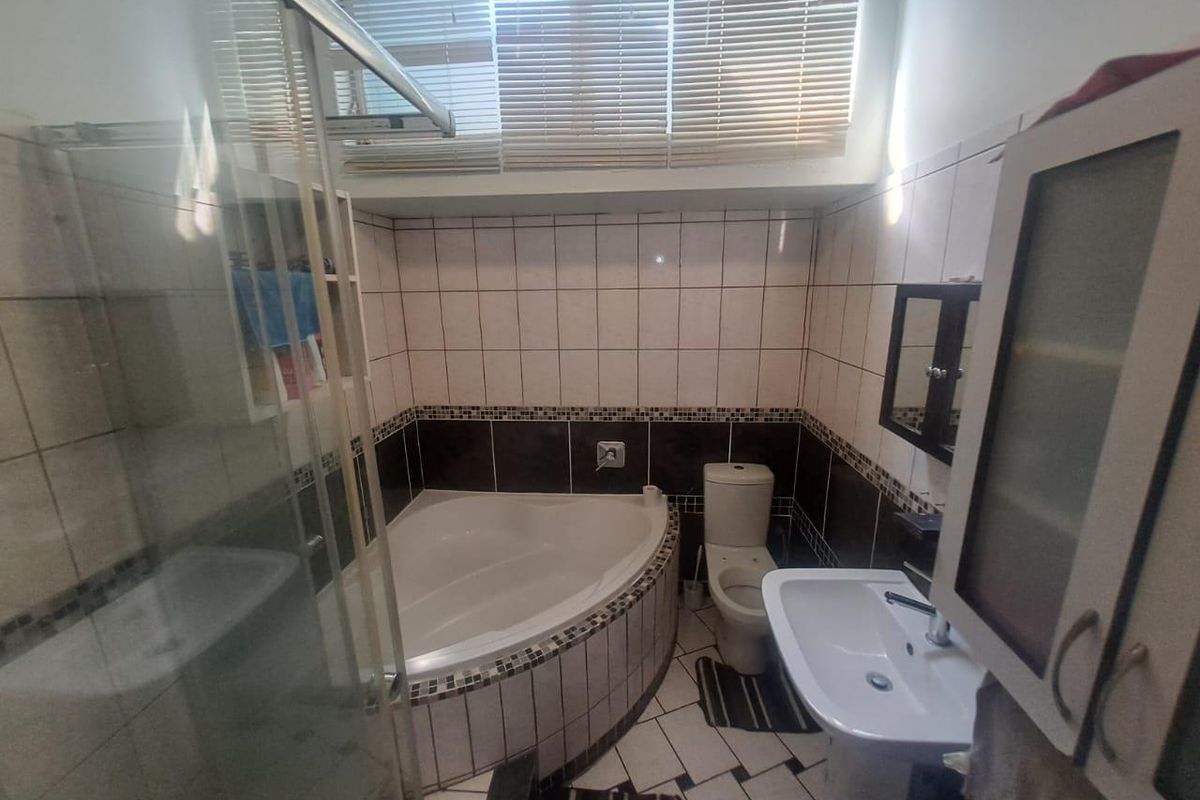 A compact bathroom featuring a corner bathtub, glass shower enclosure, pedestal basin, and toilet with tiled walls and floors.