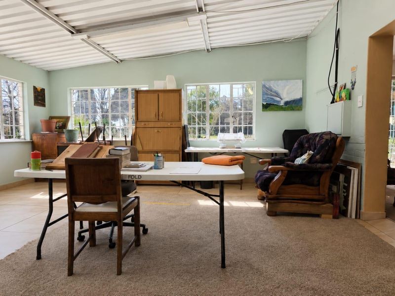 A multi-purpose living space featuring large steel-framed windows, exposed corrugated metal ceiling, and a combination of tiled and carpeted flooring.