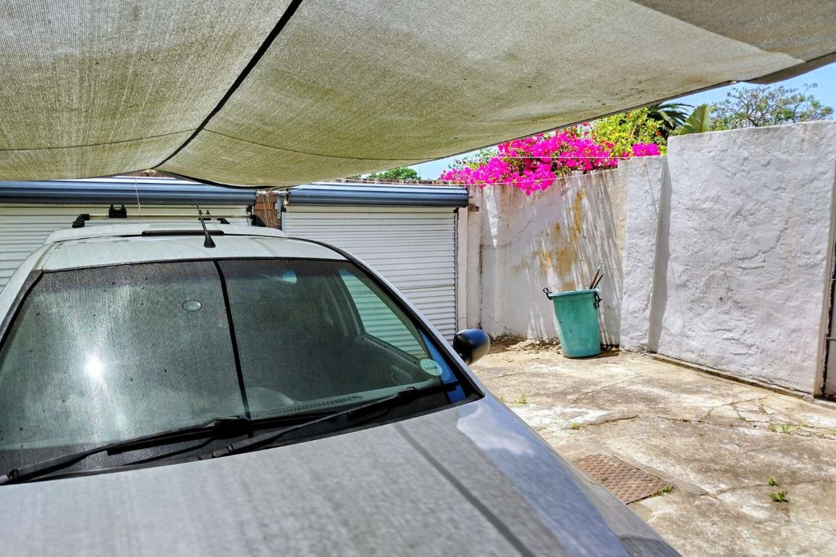Outdoor parking area featuring a shade cloth cover, concrete paving, and perimeter boundary walls with flowering bougainvillea.