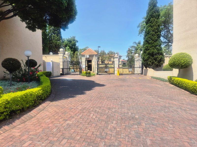 The entrance to the apartment complex features a secure gated access point with a guard house and a well-maintained paved driveway.