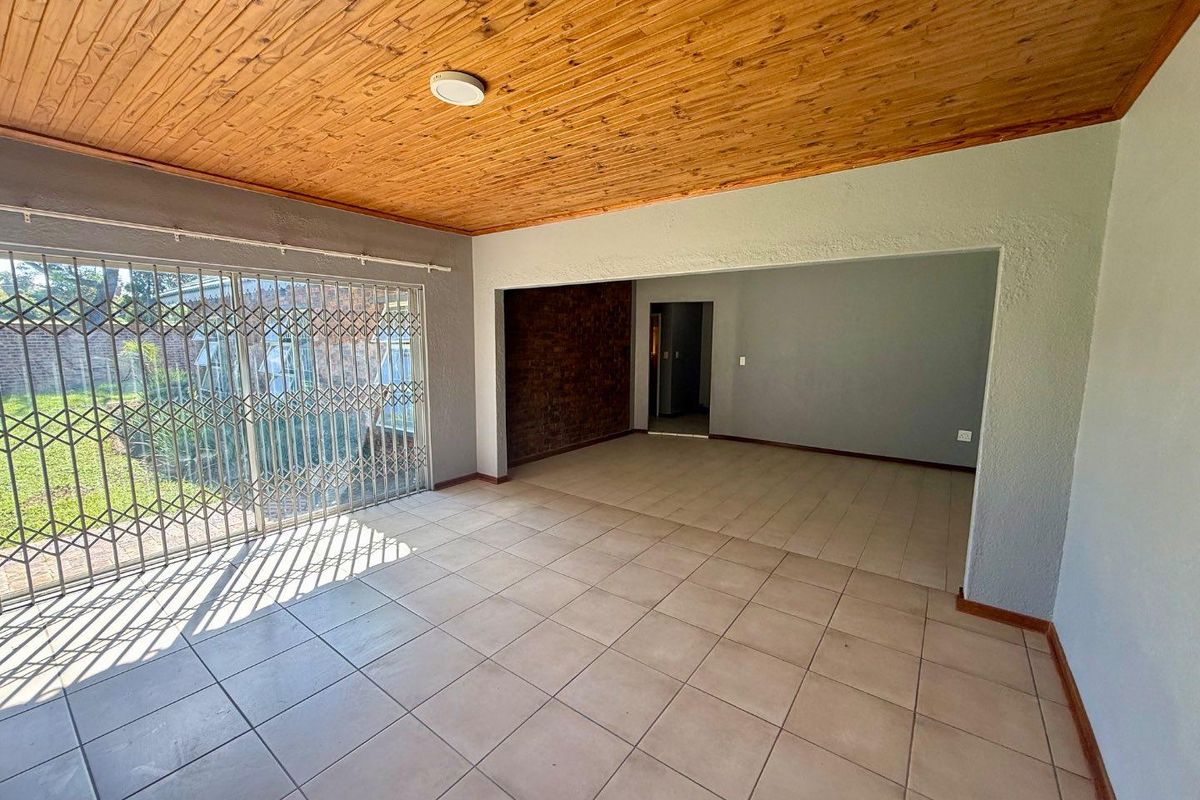 Spacious living area featuring tiled flooring, a warm timber ceiling, and a sliding glass door with security gate leading to the garden.