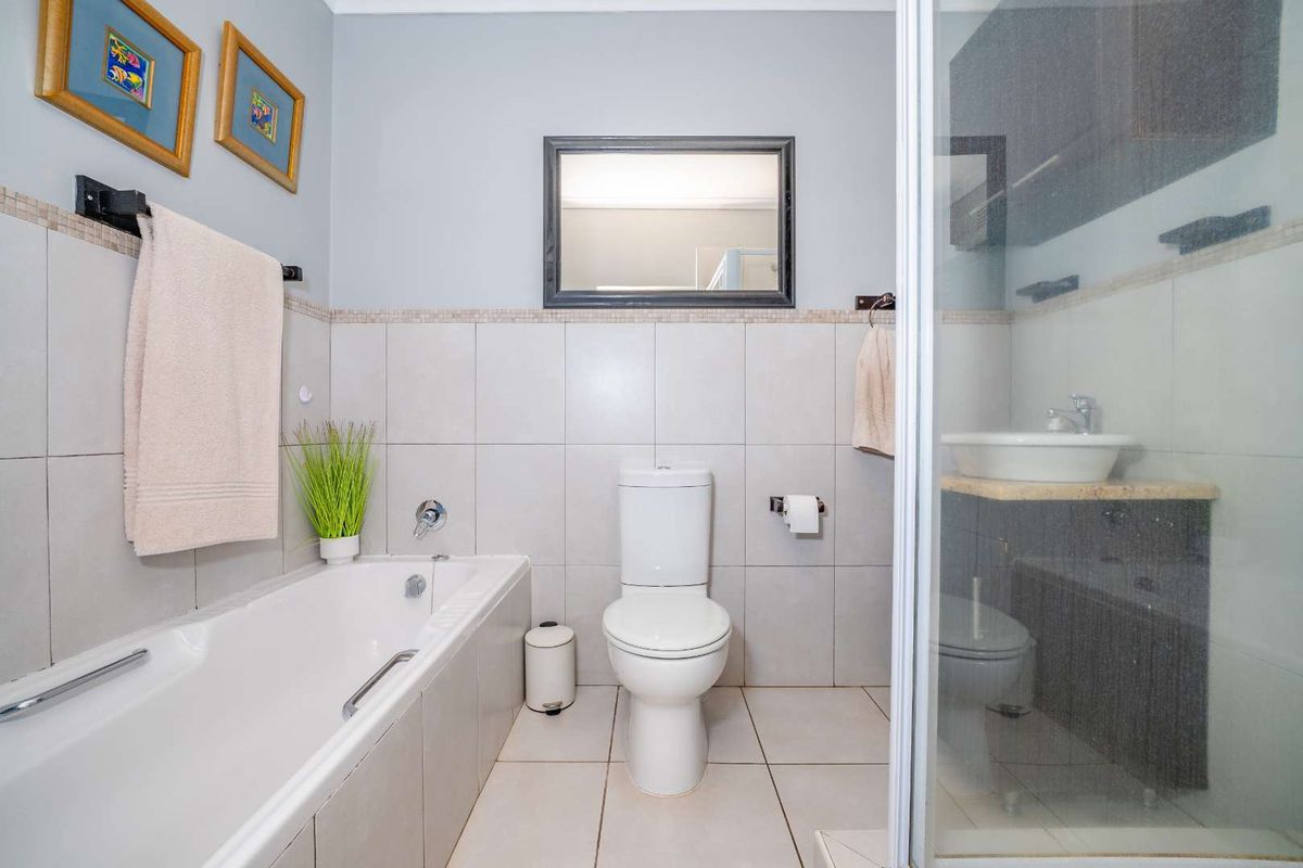 A well-maintained bathroom featuring a built-in bathtub, separate shower enclosure, toilet, and a vanity basin with neutral wall and floor tiling.