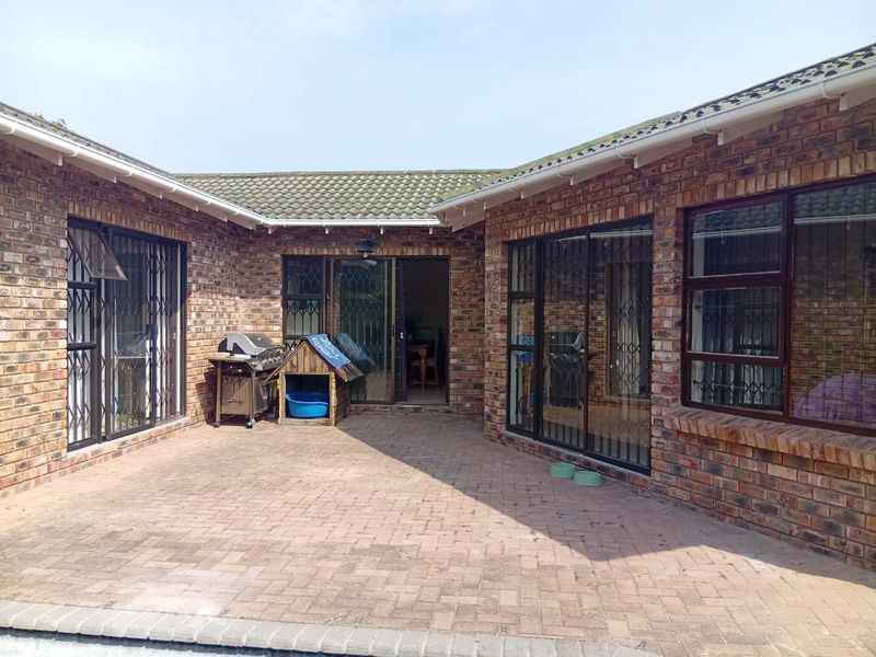 A paved outdoor patio area featuring face brick walls, sliding glass doors with security gates, and a tiled roof structure.