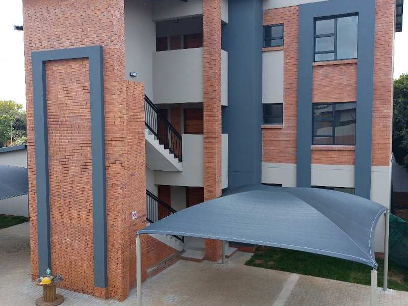 A modern three-story townhouse exterior featuring a combination of face brick and painted plaster finishes, complete with a dedicated shade cloth carport.