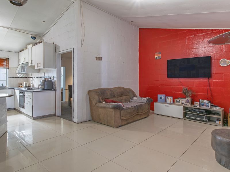 Open-plan living and kitchen area featuring tiled floors, built-in cabinetry, and a distinctive red accent wall, offering a functional layout with potential for modernization.