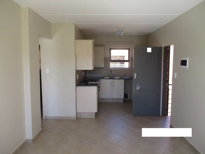 An open-plan living area featuring a compact kitchen with built-in cabinetry, laminate countertops, and tiled flooring throughout.