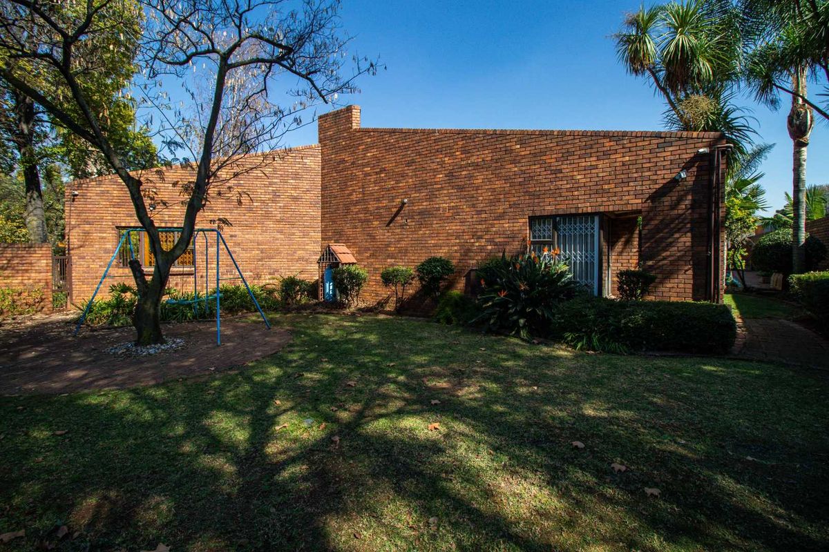 Rear view of the house featuring a face-brick facade, established garden, and paved area.