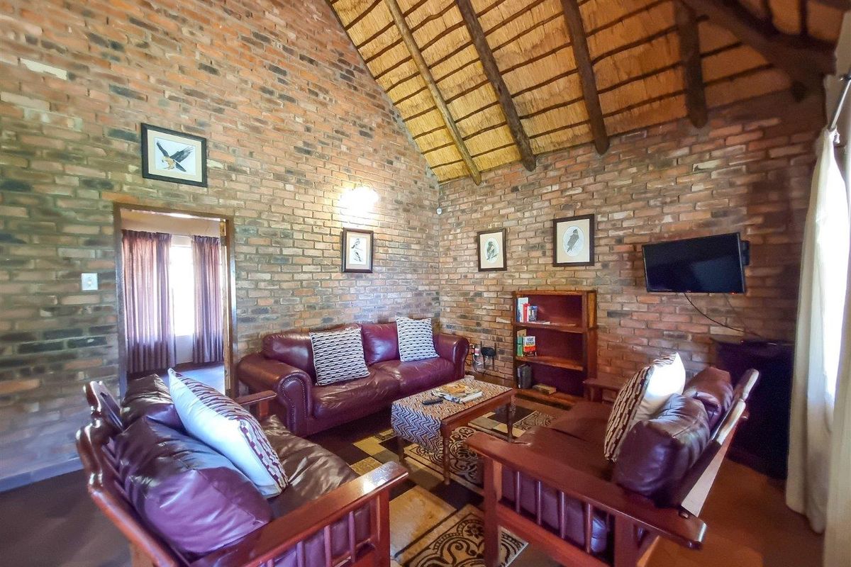 A rustic living room featuring exposed brick walls and a high vaulted thatched ceiling, creating a warm and traditional atmosphere.