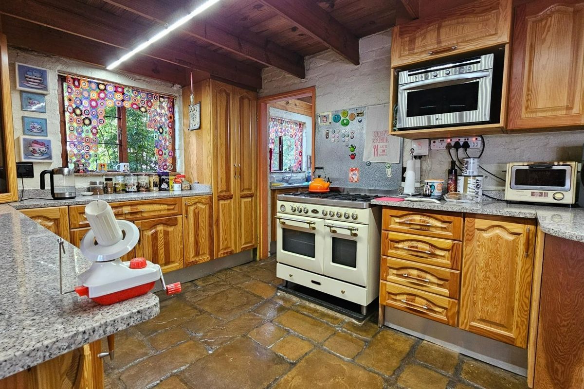 A rustic kitchen featuring timber cabinetry, granite-look countertops, a gas range stove, and exposed timber ceiling beams.