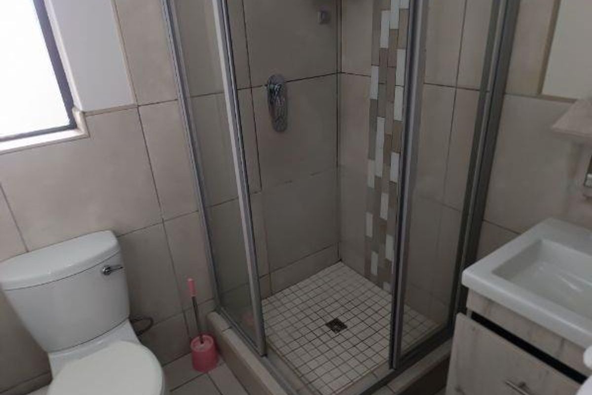 A functional bathroom featuring a glass-enclosed shower, a standard toilet, and a vanity basin with built-in cabinetry.