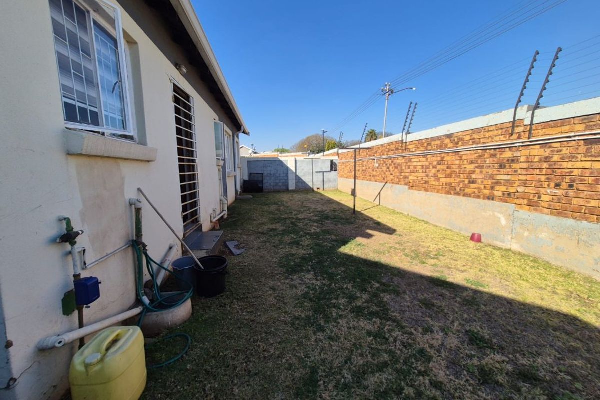 Rear garden area featuring a brick boundary wall with electric fencing, security bars on windows, and an external water tap.
