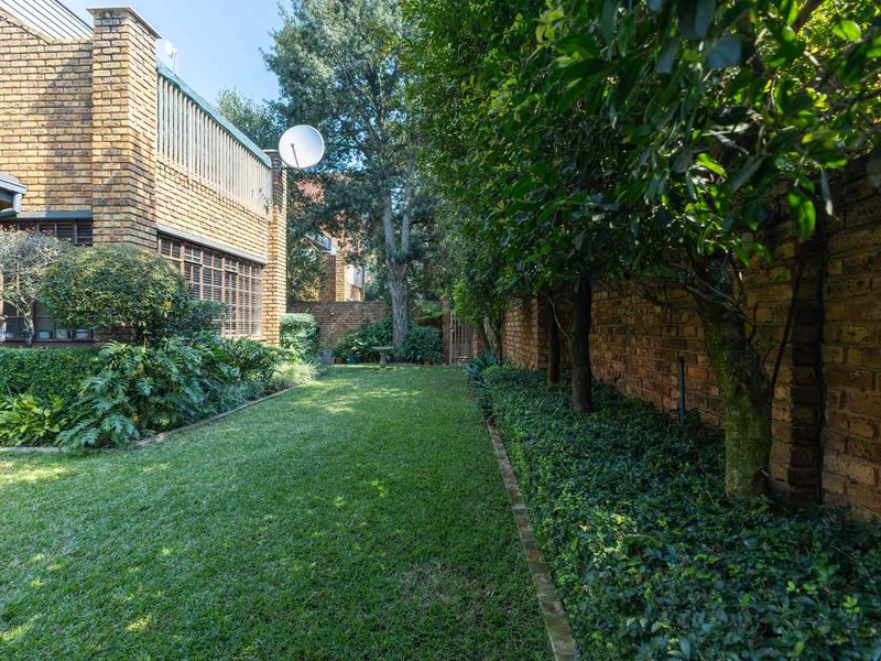 A well-maintained rear garden featuring a lush lawn, mature landscaping, and a classic face brick exterior wall of the townhouse.