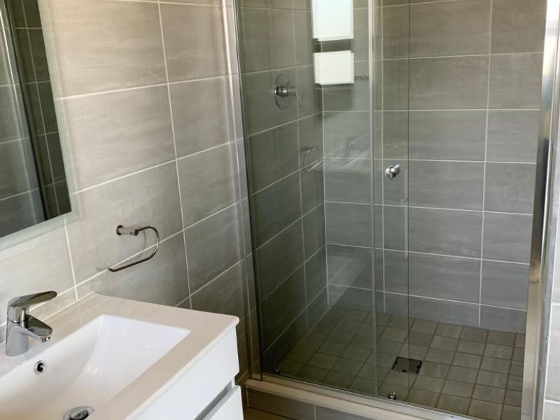 Modern bathroom featuring a sleek white vanity with basin, mixer tap, and a spacious walk-in shower with glass sliding doors and neutral wall tiling.