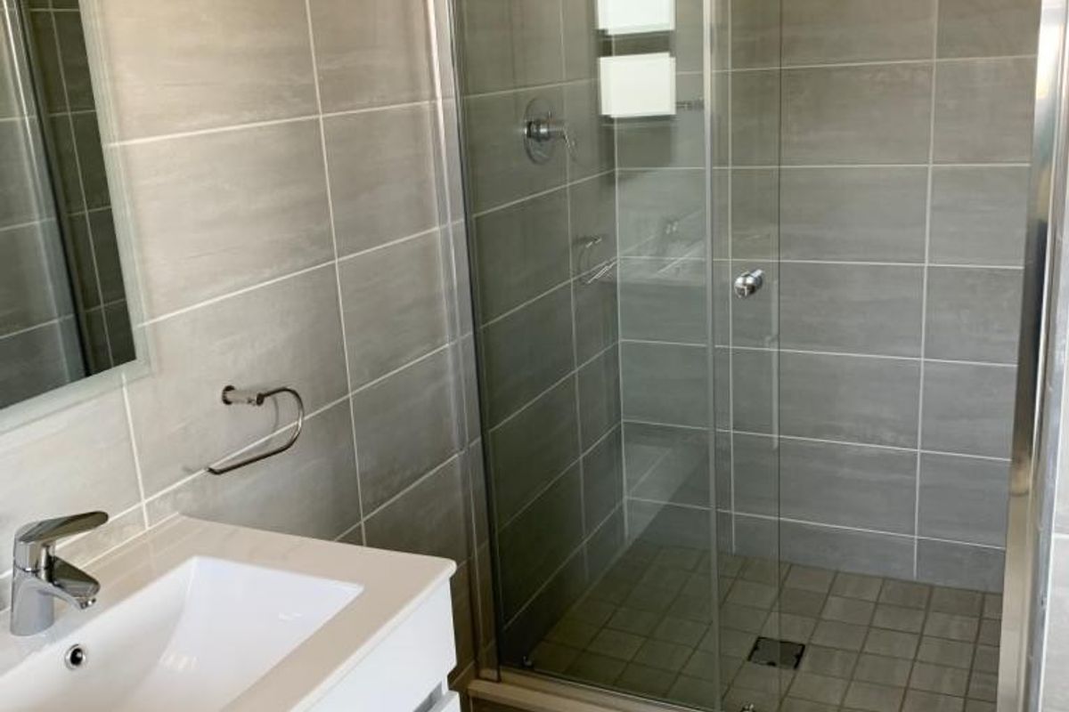Modern bathroom featuring a sleek white vanity with basin, mixer tap, and a spacious walk-in shower with glass sliding doors and neutral wall tiling.