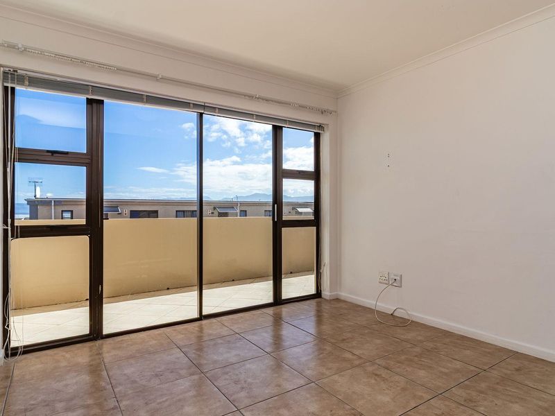 A bright, empty living area featuring tiled flooring and large sliding glass doors that open onto a private balcony with scenic views.