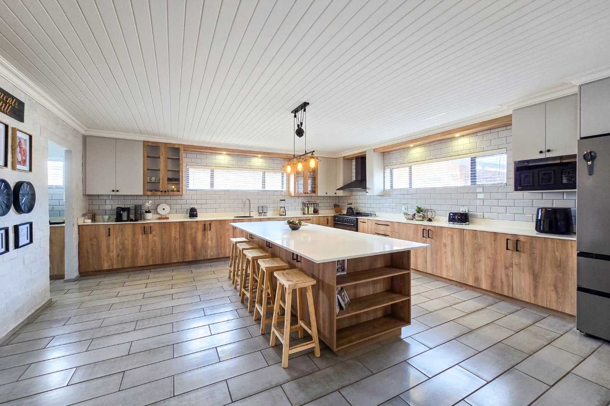Spacious modern kitchen featuring a large central island, wood-finish cabinetry, stone countertops, subway tile backsplash, and a distinctive tongue-and-groove ceiling.