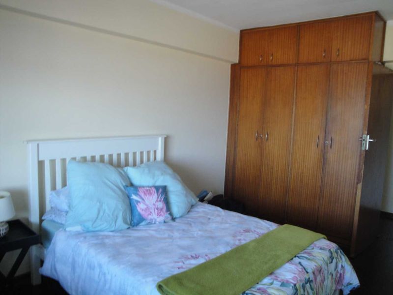 A bedroom featuring a large, floor-to-ceiling built-in wooden wardrobe with ample storage space.