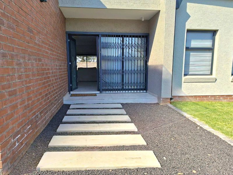 Front entrance of the townhouse featuring a modern concrete stepping stone path, brick and plastered exterior walls, and a secure sliding glass door.